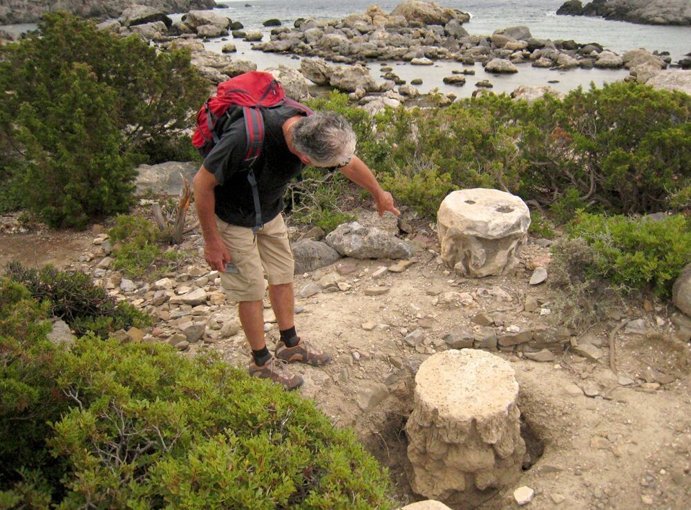 Hiker examining ancient column capitals on the rocky coast - Greece