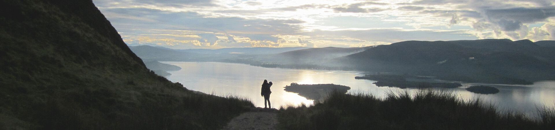 Hiker overlooking a loch at sunset - Highlands - Scotland