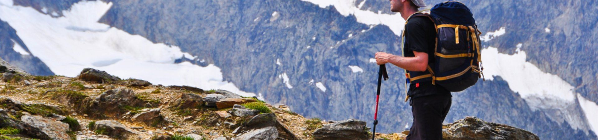 Hiker with backpack and poles facing snowy peaks - Alps