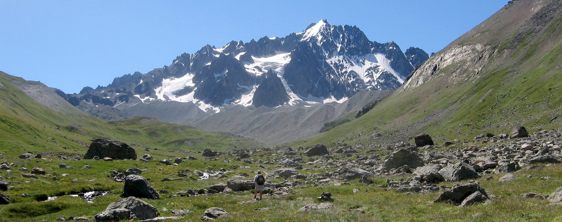 Randonneur dans un vallon herbeux face aux sommets enneigés - entre Écrins et Thabor - Alpes - France