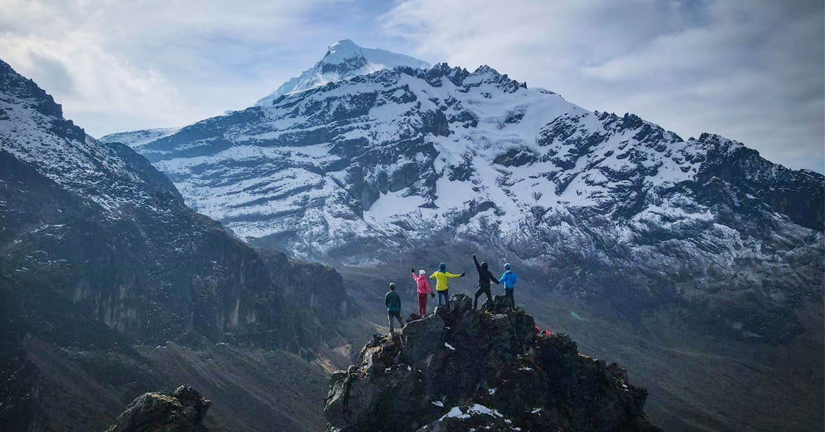 Trekkers at summit facing snow-capped volcano - Ecuador